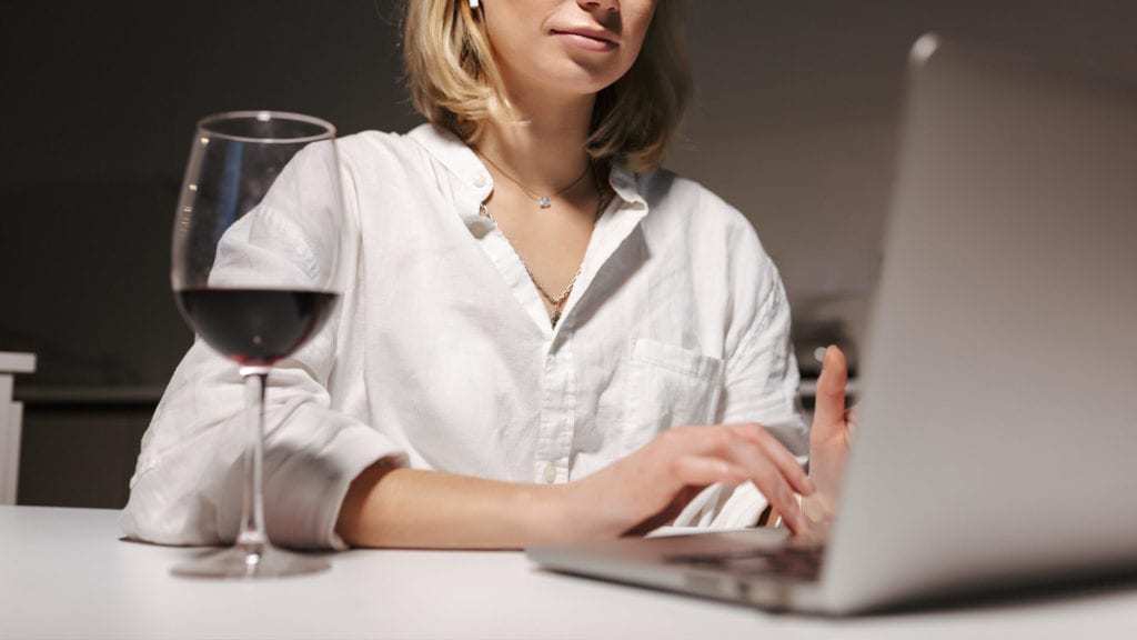 woman working on laptop and drinking red wine